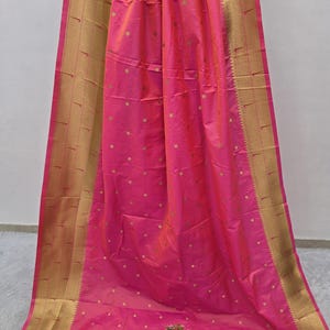K&ouml;nnte beinhalten: Ein leuchtend rosa Textil mit einem goldenen Rand und kleinen goldenen Tupfen. Der Stoff ist drapiert und zeigt seine Textur und seinen Glanz. Der goldene Rand verleiht dem Design eine elegante Note.