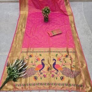 K&ouml;nnte beinhalten: Ein leuchtend pinkfarbener Sari mit goldenem Besatz und einem dekorativen Rand mit zwei Pfauen. Der Sari hat ein gepunktetes Muster und ist mit Quasten verziert. Ein kleiner Blumenstrau&szlig; und eine passende Tasche sind ebenfalls zu sehen.