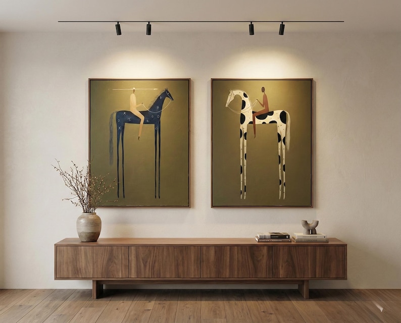 May include: Two framed art prints depicting whimsical illustrations of riders on elongated horses. One horse is dark blue with star-like accents, the other is white with black spots. Both are set against an olive-green background.