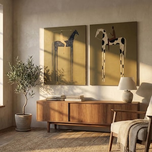 May include: Two framed art prints depict stylized horses with long legs and riders, set against a mustard-yellow background. The artwork is displayed above a wooden cabinet, with a potted olive tree and a lamp adding to the room's decor.