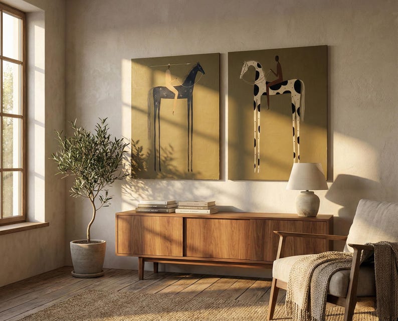 May include: Two framed art prints depict stylized horses with long legs and riders, set against a mustard-yellow background. The artwork is displayed above a wooden cabinet, with a potted olive tree and a lamp adding to the room's decor.