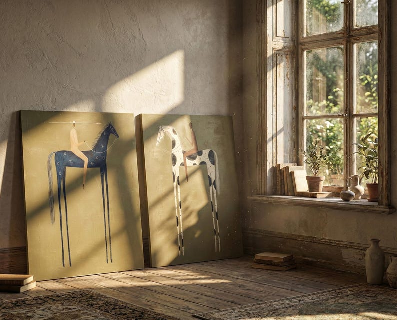 May include: Two canvas art prints leaning against a wall. One features a dark blue horse with a rider, the other a white horse with black spots. Both have elongated legs and are set against a muted background. The room has a rustic feel with a window and sunlight.