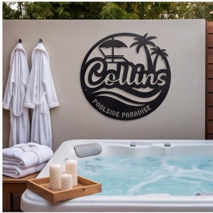 May include: A circular black metal wall sign featuring a cutout design of palm trees, a lounge chair with an umbrella, and waves. The text reads Collins and POOLSIDE PARADISE in a stylized font. The sign is mounted on a light-colored wall.
