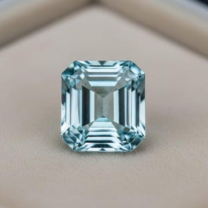 May include: A rectangular, light blue gemstone with an emerald cut. The gem is set against a neutral background. The top of the image has the text "GemoraLuxeJewels".