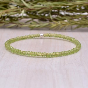 May include: A delicate bracelet featuring small, round, light green peridot gemstones. The bracelet is strung on a thin, elastic band and has a small silver bead. The gemstones are a pale, translucent green.