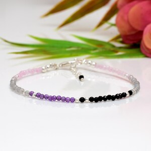 Puede incluir: Delicada pulsera de cuentas con una gradación de colores. La pulsera transiciona de rosa claro a gris, luego a morado y finalmente a cuentas negras. La pulsera está hecha con cuentas pequeñas y redondas y un cierre plateado.