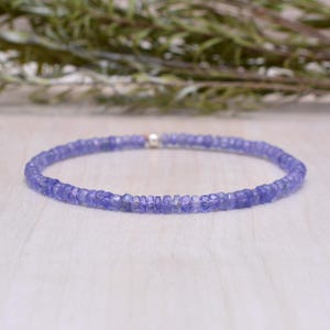 Può includere: Un delicato braccialetto composto da piccole pietre preziose sfaccettate di colore viola chiaro. Il braccialetto è assemblato con una chiusura argentata. Le pietre preziose sono di dimensioni uniformi e disposte in un motivo circolare. Il braccialetto è mostrato su una superficie di legno chiaro.