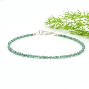 Puede incluir: Una delicada pulsera con pequeñas cuentas redondas y facetadas de esmeralda. Las cuentas son de color verde vibrante y están unidas con un cierre plateado. La pulsera se muestra sobre un fondo blanco con un toque de follaje verde.