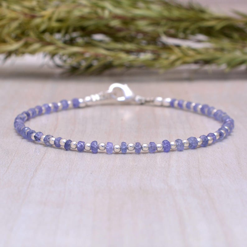 May include: A delicate bracelet featuring small, round, light purple gemstones and silver-colored beads. The bracelet is strung on a thin, flexible wire and secured with a silver-colored clasp. The gemstones are approximately 2-3 mm in diameter.