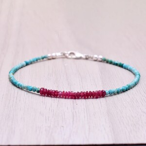 May include: A beaded bracelet with turquoise and ruby gemstones. The bracelet has a silver clasp. The turquoise beads transition to ruby beads in the centre. A simple and elegant piece of jewellery.