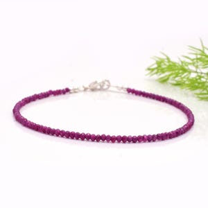 Op de afbeelding: Een fijne armband met kleine, gefacetteerde, dieproze edelstenen. De armband heeft een zilveren sluiting en wordt gepresenteerd tegen een witte achtergrond. De edelstenen zijn een levendige roze tint.
