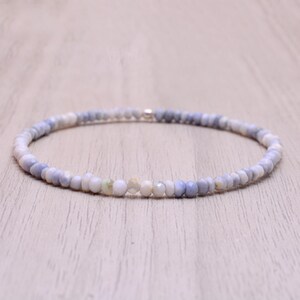 May include: A delicate bracelet composed of small, round, light blue and white beads. The beads are strung together, forming a flexible band. The bracelet is designed to be worn around the wrist and has a simple, elegant aesthetic.
