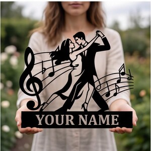Könnte beinhalten: Ein schwarzes Metallschild mit der Silhouette eines tanzenden Paares, integriert mit Noten und einem Violinschlüssel. Die Basis des Designs enthält eine rechteckige Platte mit dem Text YOUR NAME in einer fetten Serifenschrift.