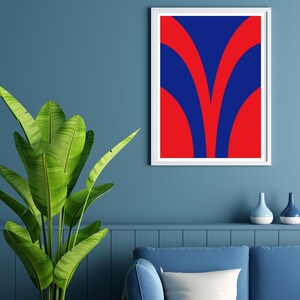 May include: A framed abstract art print with a white border. The artwork features a bold design of red and blue curved shapes. A large green plant with broad leaves is in the foreground. Two decorative vases sit on a shelf below the artwork.