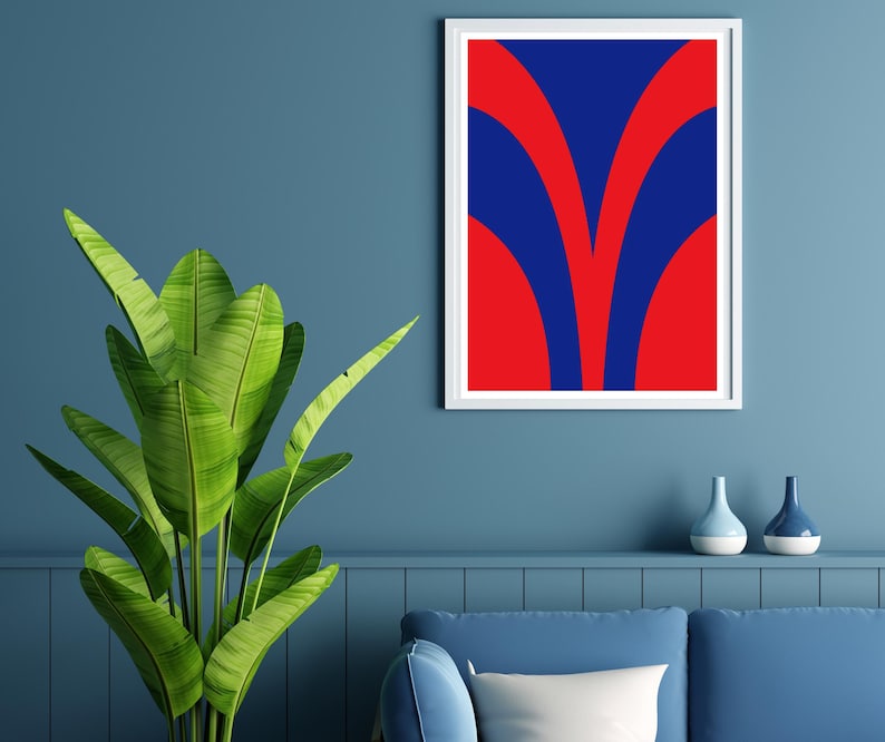 May include: A framed abstract art print with a white border. The artwork features a bold design of red and blue curved shapes. A large green plant with broad leaves is in the foreground. Two decorative vases sit on a shelf below the artwork.