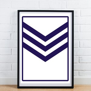 May include: Framed art print with a white background and a navy blue chevron design. The design has three horizontal chevrons within a navy blue border. The artwork is in a black frame, set against a white brick wall.