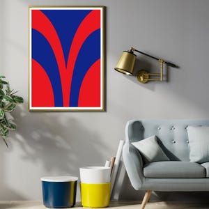 May include: A framed abstract art print with a gold frame. The artwork features a bold design of red and blue curved shapes. The print is displayed on a gray wall, with a gold-toned wall lamp and a light blue sofa visible.