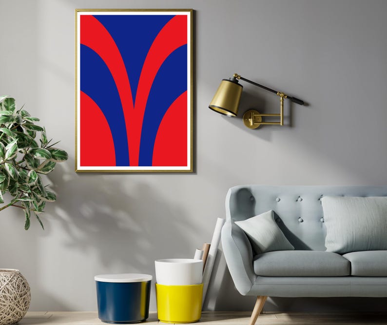 May include: A framed abstract art print with a gold frame. The artwork features a bold design of red and blue curved shapes. The print is displayed on a gray wall, with a gold-toned wall lamp and a light blue sofa visible.