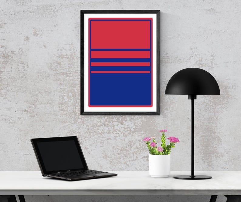 May include: A framed abstract art print with a red and blue colour block design. The artwork features a red upper section, blue lower section, and three horizontal red stripes. A black desk lamp, laptop, and small potted flowers are also visible.