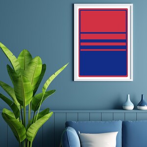 May include: A framed abstract art print with a red and blue geometric design. The artwork features a red upper section, blue lower section, and horizontal blue stripes. The print is displayed on a blue wall, with a plant and decorative vases in the foreground.