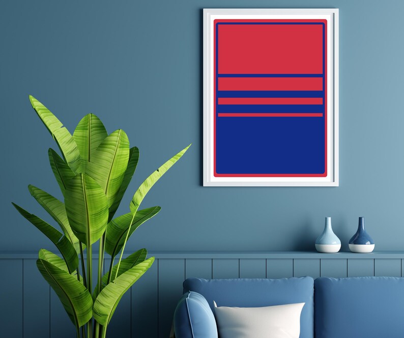 May include: A framed abstract art print with a red and blue geometric design. The artwork features a red upper section, blue lower section, and horizontal blue stripes. The print is displayed on a blue wall, with a plant and decorative vases in the foreground.