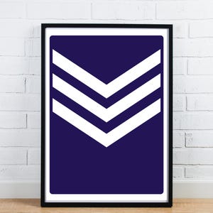 Puede incluir: Impresión artística enmarcada con un fondo azul marino y tres chevrones blancos que apuntan hacia abajo. La obra de arte está enmarcada en negro y montada en una pared de ladrillos blancos.