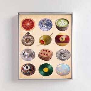 May include: A framed art print featuring a grid of twelve circular objects on a beige background: a blood orange slice, Earth, a matcha latte, a pocket watch, a pimento-stuffed olive, a number seven billiard ball, a disco ball, a wooden die, a silver coin, an eight ball, a green vinyl record, and an iridescent opal.
