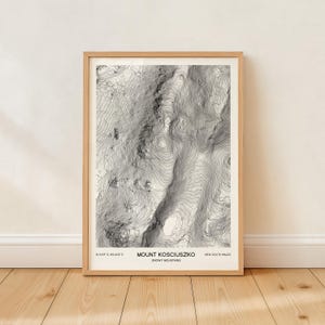 Peut inclure: Impression encadrée d'une carte topographique du Mont Kosciuszko dans les Snowy Mountains, Nouvelle-Galles du Sud. La carte en noir et blanc présente des courbes de niveau et le nom et les coordonnées de la montagne. L'impression est dans un cadre en bois brun clair.