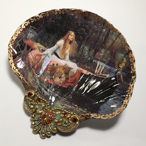 May include: A decorative seashell dish with a gold trim and a vintage image of a woman in a boat. The dish has a gold-colored metal embellishment with red and blue jewels.