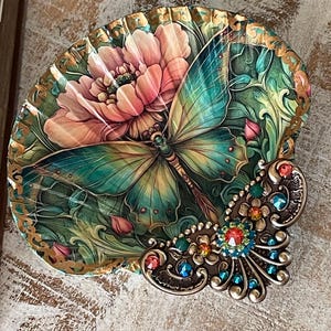 May include: A decorative seashell dish with a painted butterfly and flower design. The shell is accented with a jeweled butterfly embellishment.