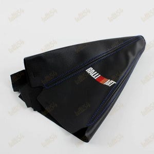 May include: Black leather car gear stick gaiter with blue stitching. The gaiter has the "RALLI ART" logo in white, red, and orange. Designed to fit a car's gear shift lever.