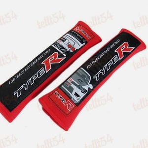 Puede incluir: Dos fundas rojas para cinturones de seguridad con paneles negros con el texto "TYPE R" e ilustraciones de coches. Las fundas también tienen el texto "FOR TRACK AND RACE USE ONLY".