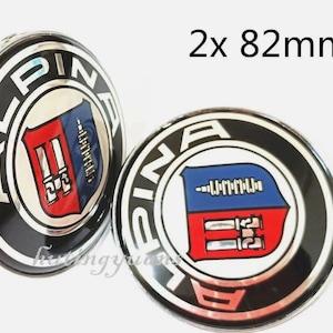 K&ouml;nnte beinhalten: Zwei Alpina-Radnabenabdeckungen, jeweils 82 mm im Durchmesser. Die Kappen sind schwarz mit silbernem Rand und dem Alpina-Logo in Wei&szlig;. Das Logo zeigt ein rot-blaues Wappen.