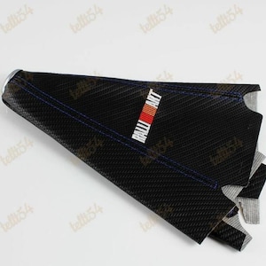 May include: Black carbon fibre car part with blue stitching and the "RALLIART" logo in white, red, and orange. The part has a textured surface and a silver metal ring at the top. The item is angled, showing its interior.