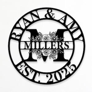 May include: A circular black metal wall sign featuring the names RYAN & AMY at the top, the letter M in the centre with floral illustrations, the name MILLERS on a horizontal bar, and the text EST. 2025 at the bottom of the circular frame.