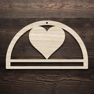 Może przedstawiać: Jasnobrązowe drewniane wycięcie przedstawiające serce w łukowatej ramie z poziomym paskiem na dole. Projekt ma mały otwór do zawieszenia. Tło to ciemnobrązowe usłojenie drewna.