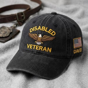 May include: A black baseball cap featuring an embroidered eagle graphic with the yellow text "DISABLED VETERAN" above and below it. The side of the cap displays a small American flag patch with the name "DAVID" embroidered in yellow underneath.