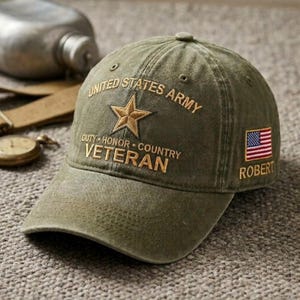 May include: An olive green baseball cap featuring embroidered text that reads UNITED STATES ARMY, DUTY HONOR COUNTRY, and VETERAN. A gold star is centred above the text. The side displays an American flag patch with the name ROBERT below it.
