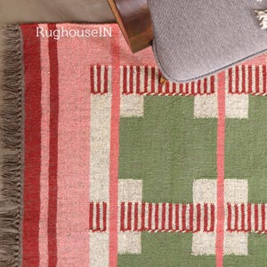 May include: A colorful woven rug with a geometric pattern. The rug features stripes of red, pink, and white, with a green section and white and red block designs. The text "RughouseIN" is visible on the rug.