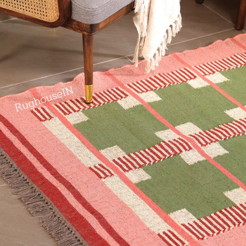 May include: A rectangular rug with a geometric pattern in shades of pink, green, and red. The rug has a fringed edge and the text "RughouseIN" is visible. The rug is partially under a wooden chair.