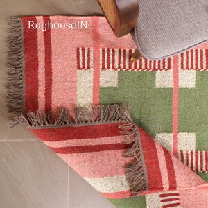 May include: A colorful rug with a geometric pattern in shades of red, pink, green, and white. The rug has a fringed edge and is partially rolled up, revealing the underside. The text "RughouseIN" is visible on the rug.