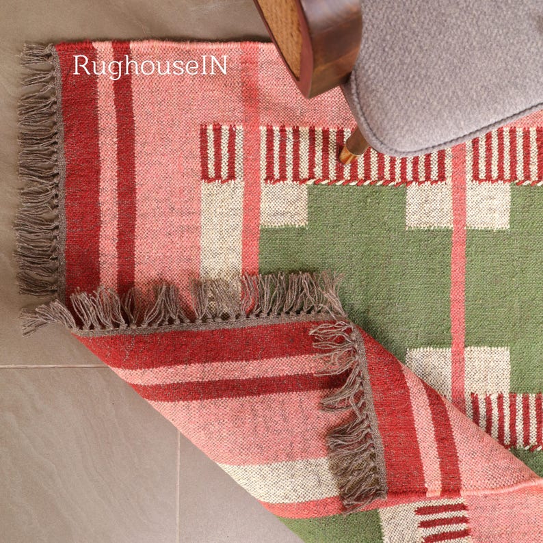 May include: A colorful rug with a geometric pattern in shades of red, pink, green, and white. The rug has a fringed edge and is partially rolled up, revealing the underside. The text "RughouseIN" is visible on the rug.