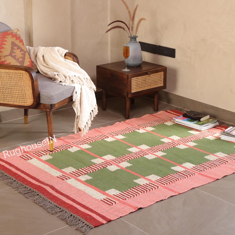 May include: A rectangular area rug with a geometric pattern in shades of green, pink, and white. The rug has a fringed edge and is placed on a tiled floor. The design features a grid-like pattern with alternating colors.