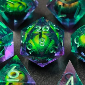 May include: Close-up of several polyhedral dice. The dice are transparent with a green and purple color scheme. The numbers are white. The dice are for tabletop role-playing games.