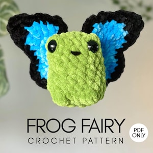 May include: A green crocheted frog with black and blue wings. The frog has large black eyes and a small smile. The text "FROG FAIRY CROCHET PATTERN" is displayed below the frog.