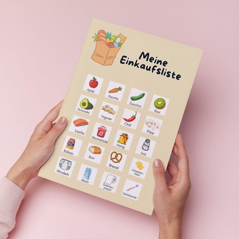 Może przedstawiać: Beżowa lista zakup&oacute;w zatytułowana "Meine Einkaufsliste" czarnym pismem, trzymana w dłoniach na r&oacute;żowym tle. Lista zawiera ilustracje artykuł&oacute;w spożywczych, takich jak jabłko, awokado i cukinia. Lista zawiera tekst "Apfel", "Karotte", "Zucchini", "Kiwi", "Avocado", "Ingwer", "Chili", "Pilze", "Lachs", "Marmelade", "Honig", "Salz", "Kakao", "Brot", "Brezel", "Scheiben-k&auml;se", "Windeln", "Milch", "Toilettenpapier" i "Zahnb&uuml;rste".