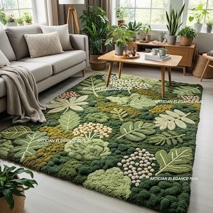 Könnte beinhalten: Ein grüner und beiger Teppich mit botanischem Thema und verschiedenen Blatt- und Blumenmustern. Der Teppich befindet sich in einem Wohnzimmer mit Sofa, Couchtisch und Pflanzen. Der Text "ARTICIAN ELEGANCE RUG" ist auf dem Teppich aufgedruckt.