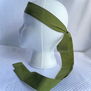 May include: A green headband with a long tail that can be tied in a bow. The headband is made of a soft, cotton fabric.