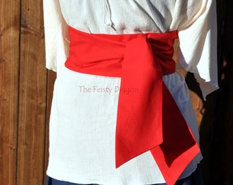 May include: A white peasant blouse with a red sash tied around the waist. The sash is tied in a bow at the front. The blouse has a gathered neckline and long sleeves. The sash is tied in a bow at the front. The blouse is worn over a dark blue skirt.