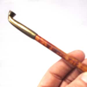 May include: A vintage pipe tool with a brass end and a wooden handle. The tool is held against a white background. The handle has a brown and orange mottled pattern.